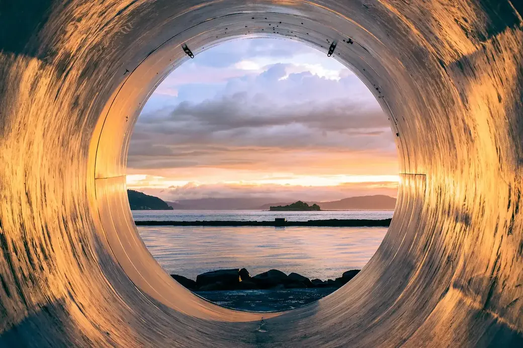 Blick durch eine gro&szlig;e R&ouml;hre auf Meer und Sonnenuntergang